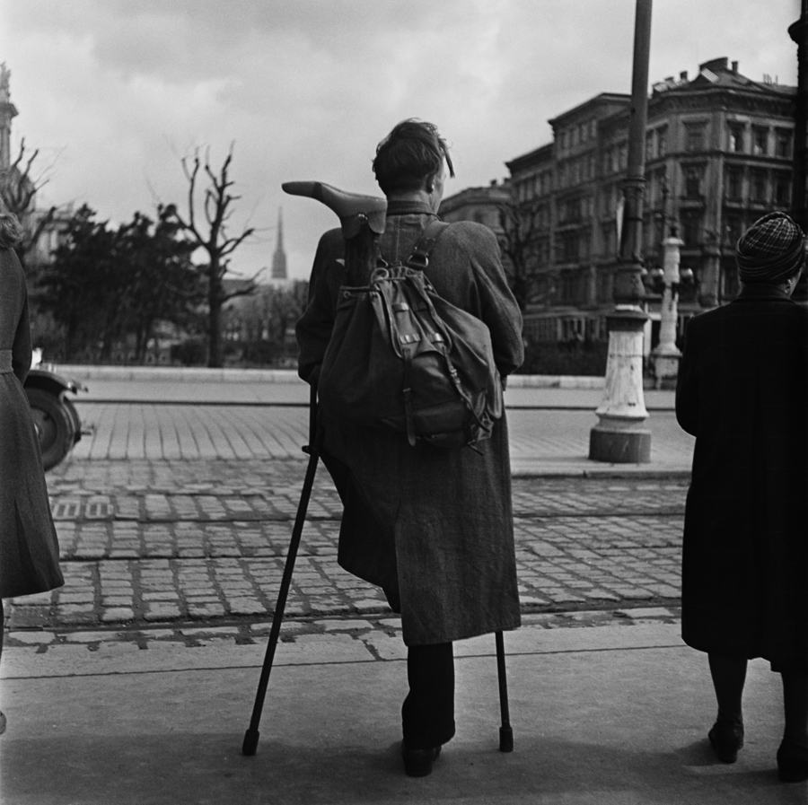 A one-legged man waits to cross a road in Vienna, a false leg sticks out of the knapsack on his back. Original Publication: In black and white book  (Photo by Ernst Haas/Getty Images)